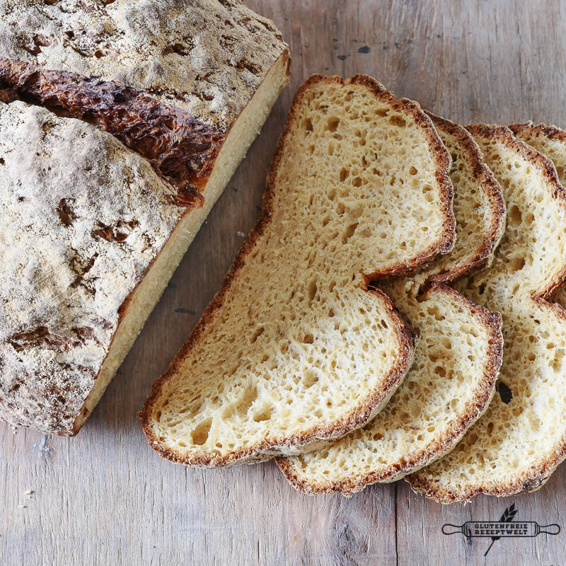 Ein rustikales Brot liegt auf einer Holzunterlage, mehrere Scheiben sind abgeschnitten und fächerförmig angeordnet, sodass man die goldgelbe, luftige Krume und die knusprige Kruste sehen kann.