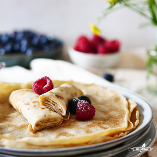 Dünner Pfannkuchen auf einem Teller, belegt mit Himbeeren und Heidelbeeren, mit zusätzlichen Beeren im Hintergrund - hergestellt mit Ruuts feinstem Weizenmehl.